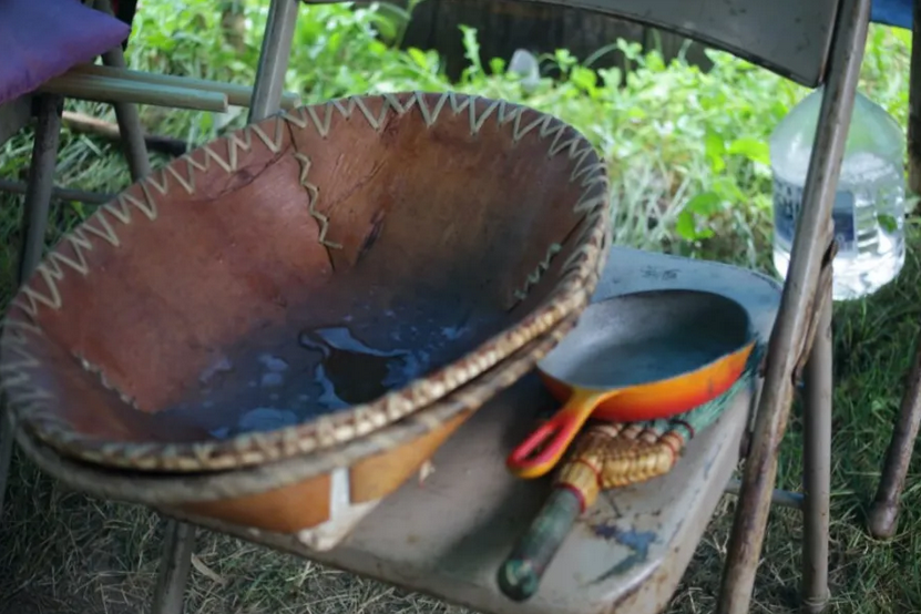 Two hand-made baskets, a small cast iron frying pan, and a wisk broom sitting on a folding chair.