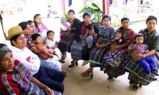 Mayan women and their children sit and listen to a presentation.
